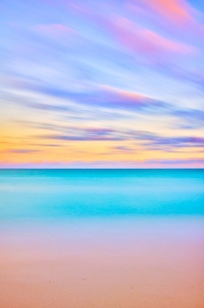Песчаная полоска у берега, бирюзовая глубина моря и розовые облака на желтеющим закатом 