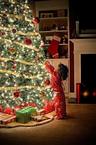 Ребенок в ночной пижаме цвета костюма Санты Клауса наряжает Рождественскую Елку
