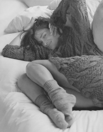 Девушка одетая в вязанную кофту, лежит среди подушек