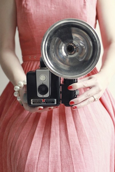 Девушка с жемчужным браслетом и фотоаппаратом со вспышкой в красном платье